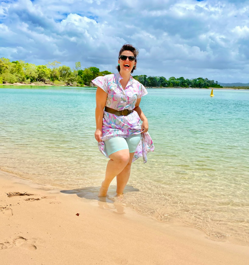 Hayley wearing Aqua Island Time Skanties showing them in the aqua water on the beach with a light colored sundress to emphasize how gorgeous the aqua color is next to aqua beach water. The joy can be seen in her face being able to wear a dress at the beach with comfort and confidence